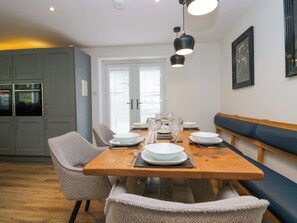 A dining area with a wooden table set for four, surrounded by chairs and a bench. - Rayrigg on the Lakes (Windermere)