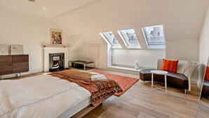 Et moderne soveværelse med en stor seng, pejs, sofa og ovenlys.