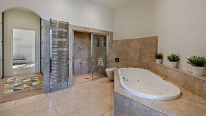 Et moderne badeværelse med et stort badekar, en bruseniche og et toilet.