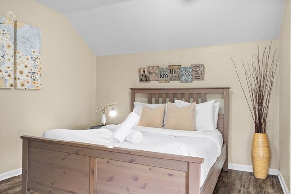 A neatly made bed with a wooden headboard, a bedside table with a lamp, and a wall-mounted sign above the bed.