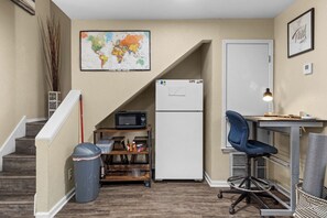A compact kitchenette with a microwave, refrigerator, and a small table with a chair. A map is displayed on the wall, and a trash bin is visible.