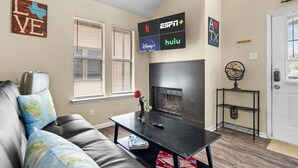 Een woonkamer met een open haard, een bank, een salontafel en een televisie aan de muur met de logo's van ESPN, Disney+ en Hulu.
