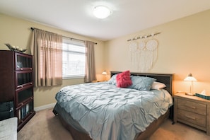 Un dormitorio con cama, mesita de noche, lámpara, ventana con cortinas y un adorno en la pared.