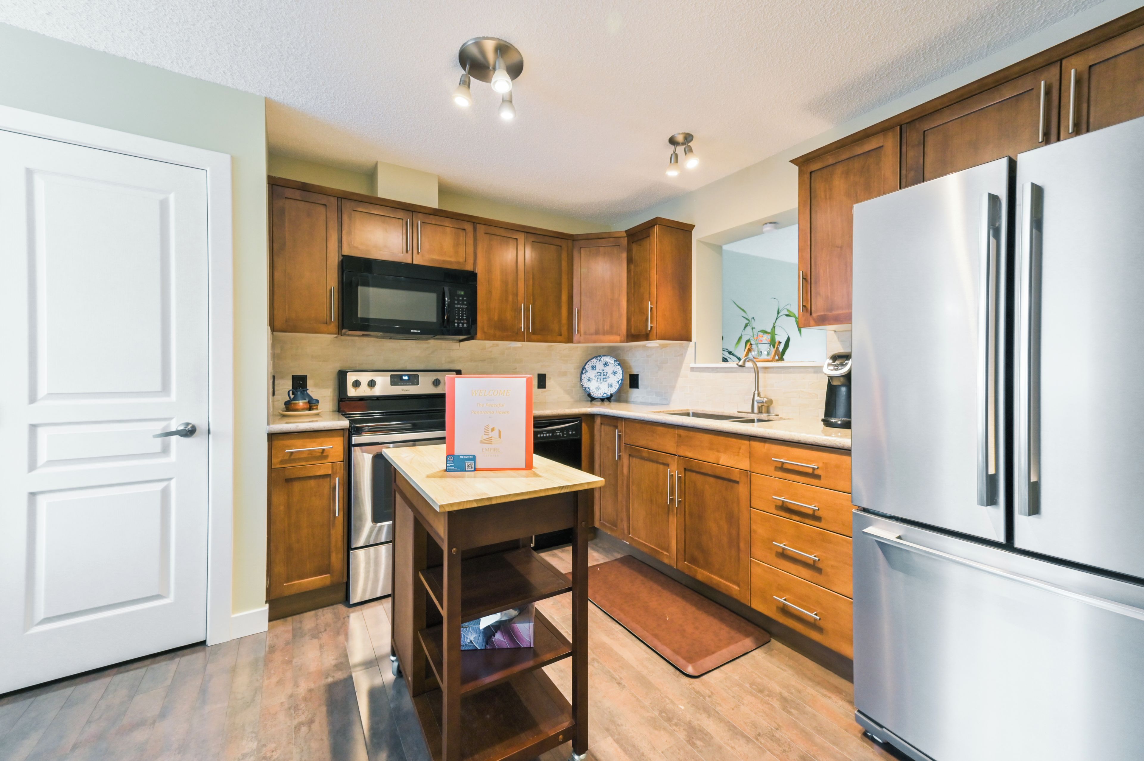 A modern kitchen with wooden cabinets, stainless steel appliances, and a welcome sign.