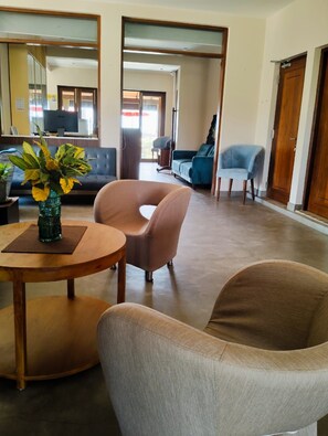 A modern living room with a round wooden table, two armchairs, a sofa, and a large mirror.