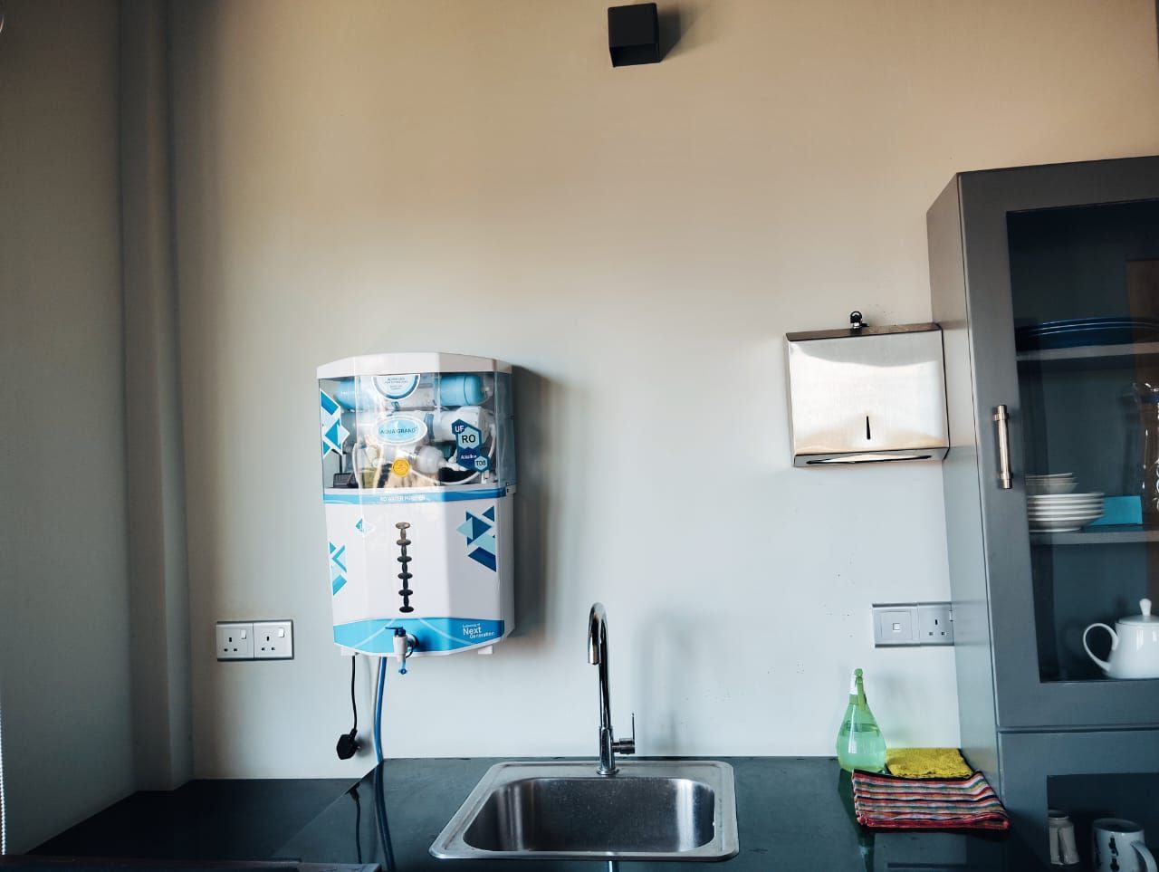 Una cocina con dispensador de agua, un lavabo y un armario con vajilla.
