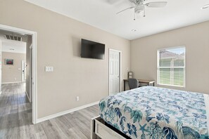 A bedroom with a bed, a desk, a chair, a television, and a window with blinds. - Blue Lobster Lodge | Beach Hair, Zero Cares (Bolivar Peninsula)