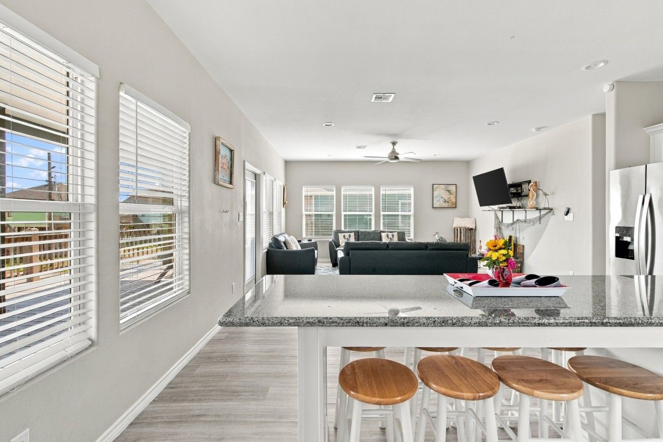 A modern kitchen with a central island, bar stools, a flat-screen TV, and a refrigerator.