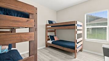 Une chambre avec deux lits superposés, une fenêtre avec des stores et un plancher de couleur claire.