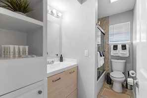 Casa de banho moderna com toucador branco, espelho, lavatório e sanita.