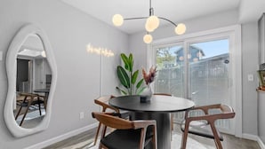 Un coin repas comprenant une table ronde, quatre chaises, un miroir, une plante et un luminaire suspendu au plafond.