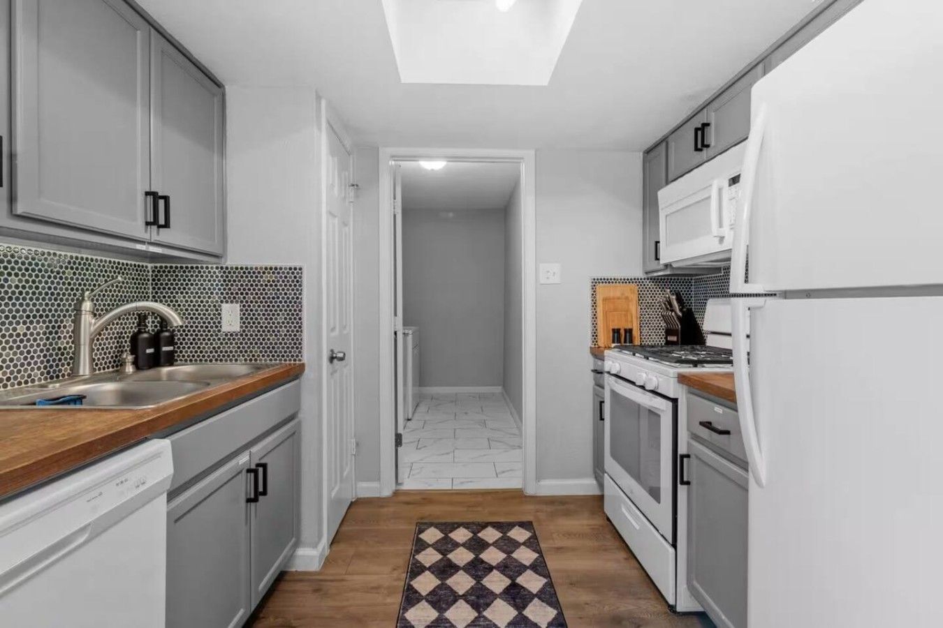 A narrow kitchen with white cabinets, a wooden countertop, a gas stove, and a microwave.