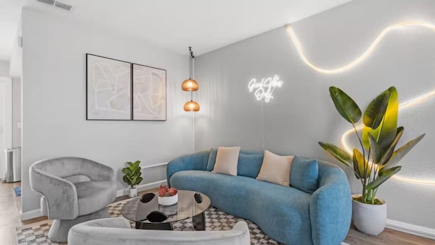 Un salon moderne avec un canapé bleu, un fauteuil gris, une table basse ronde et une plante en pot.