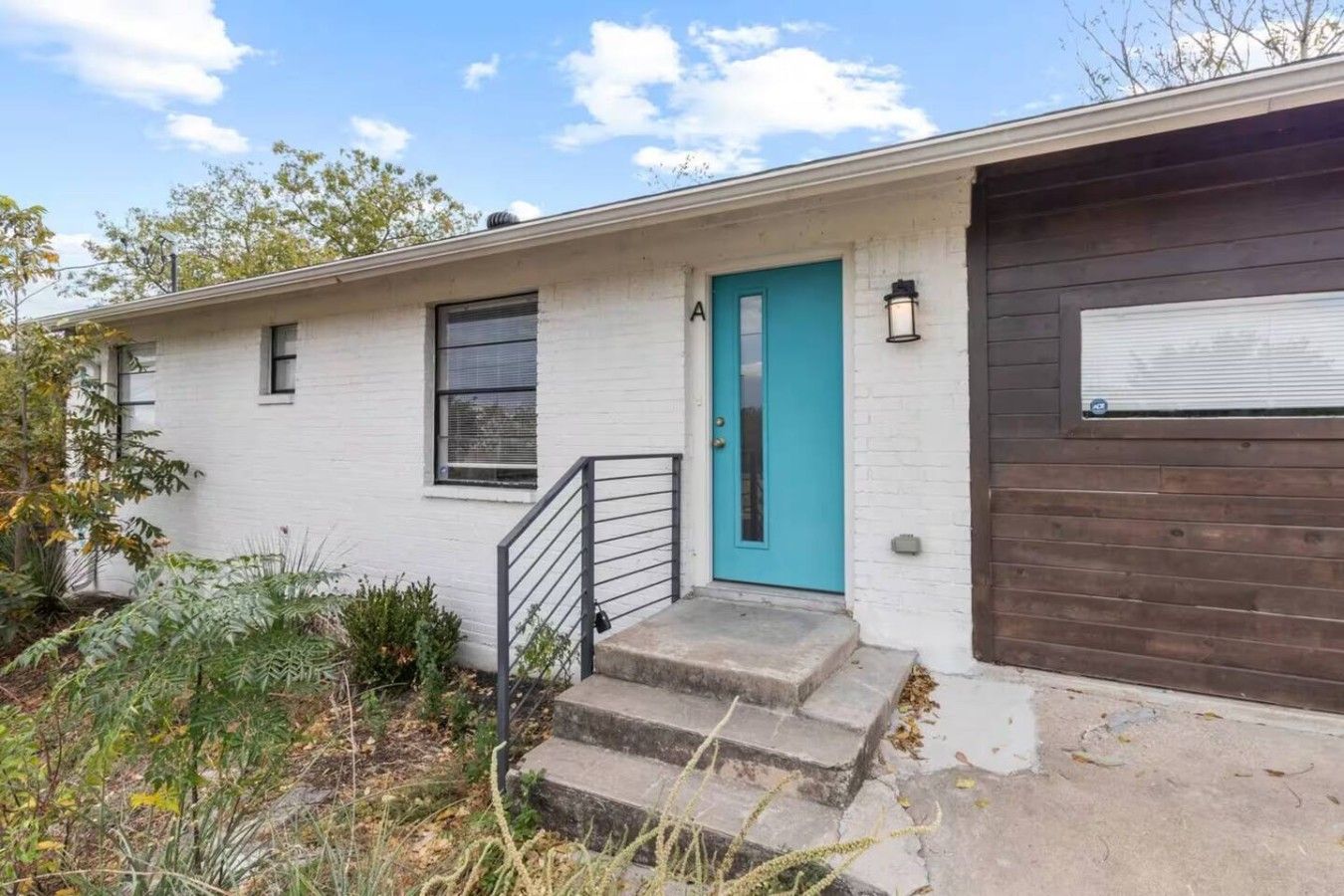 A single-story house with a white exterior, a teal door, and a dark brown garage door.