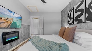 Une chambre à coucher avec un lit, un téléviseur fixé au mur et une porte donnant sur une autre pièce.