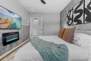 Quarto com cama, televisão fixada na parede e porta para outro cômodo.