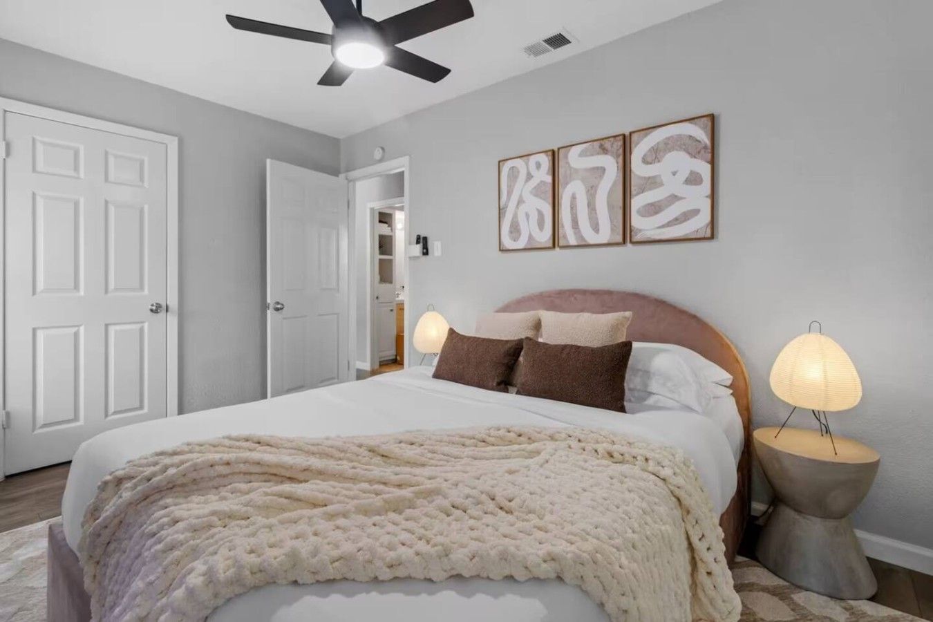 A bedroom with a bed, a ceiling fan, bedside lamps, and artwork on the wall.