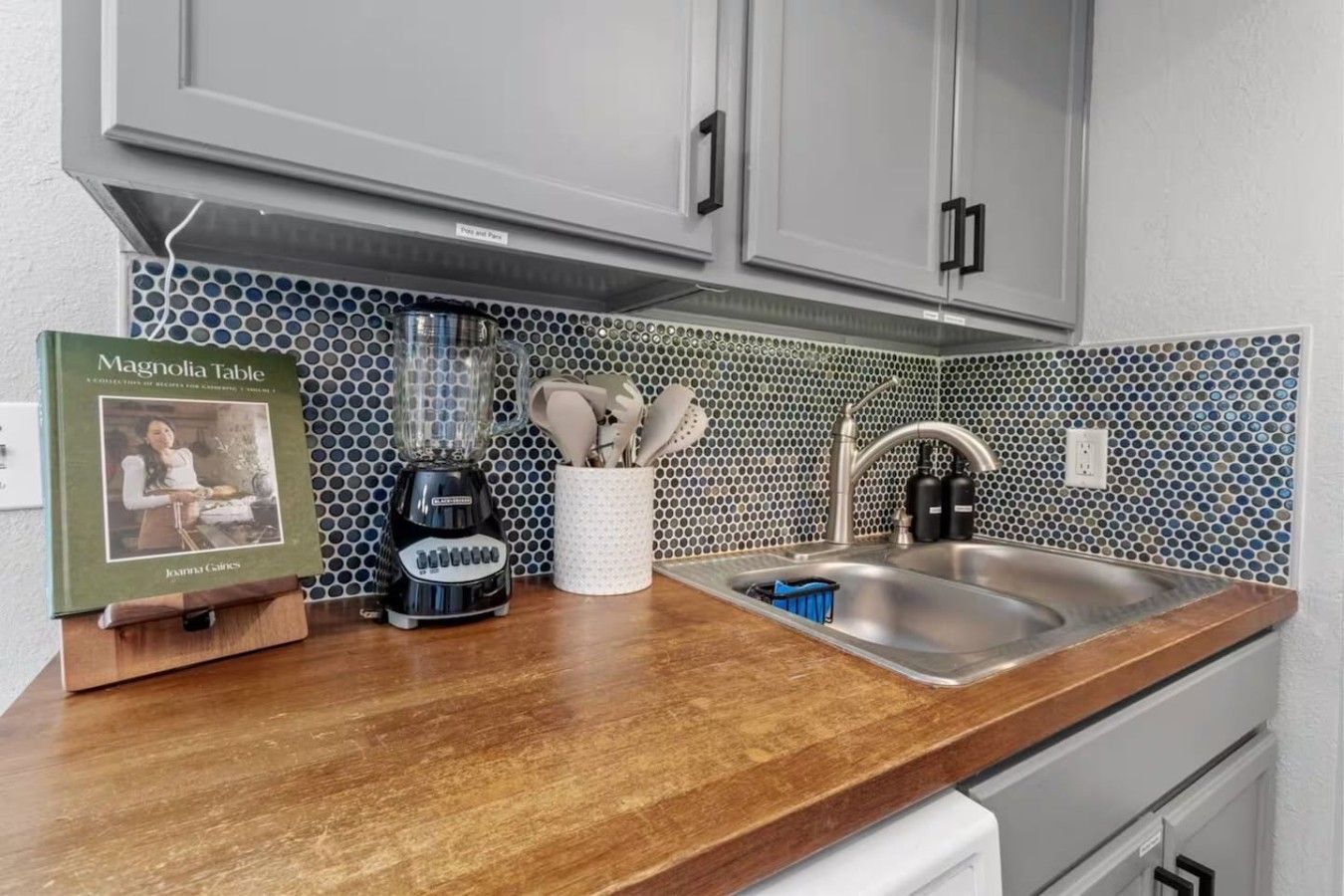 A kitchen with a wooden countertop, a blender, a cookbook, and a sink.