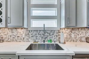 A modern kitchen with a stainless steel sink, grey cabinets, and a patterned backsplash. - Royal Beach Retreat | Sleeps 16 | 4Bd/2.5Bth (Bolivar Peninsula)