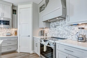 A modern kitchen with white cabinetry, a built-in oven, a microwave, and a blender on the counter. - Royal Beach Retreat | Sleeps 16 | 4Bd/2.5Bth (Bolivar Peninsula)