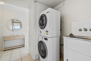 A compact laundry room with a stacked washer and dryer, a small vanity with a mirror, and a sink with faucets. - Anacapri Vista Panoramic Views in Central Paradise (Surfers Paradise)