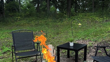 A fire pit with flames, surrounded by outdoor furniture and a gravel ground.