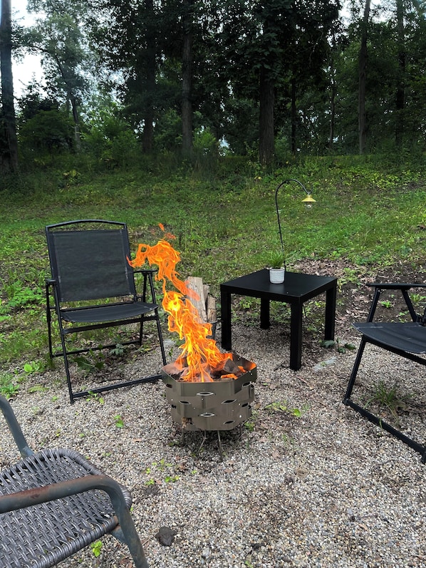 A fire pit with flames, surrounded by outdoor furniture and a gravel ground.
