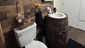 Un baño con pared de madera, un inodoro, un lavabo con recipiente de madera y un espejo.