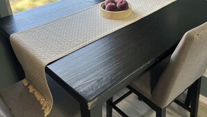 Una mesa de comedor con un posavasos tejido, un cuenco de fruta y un banco con cojín.