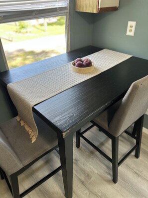 A dining table with a woven placemat, a bowl of fruit, and a bench with a cushion. - Cozy cottage cabin with lake and beach access (Albion)