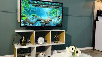 A living room with a television displaying a scenic image, a white shelf with decorative items, and a fluffy white rug.