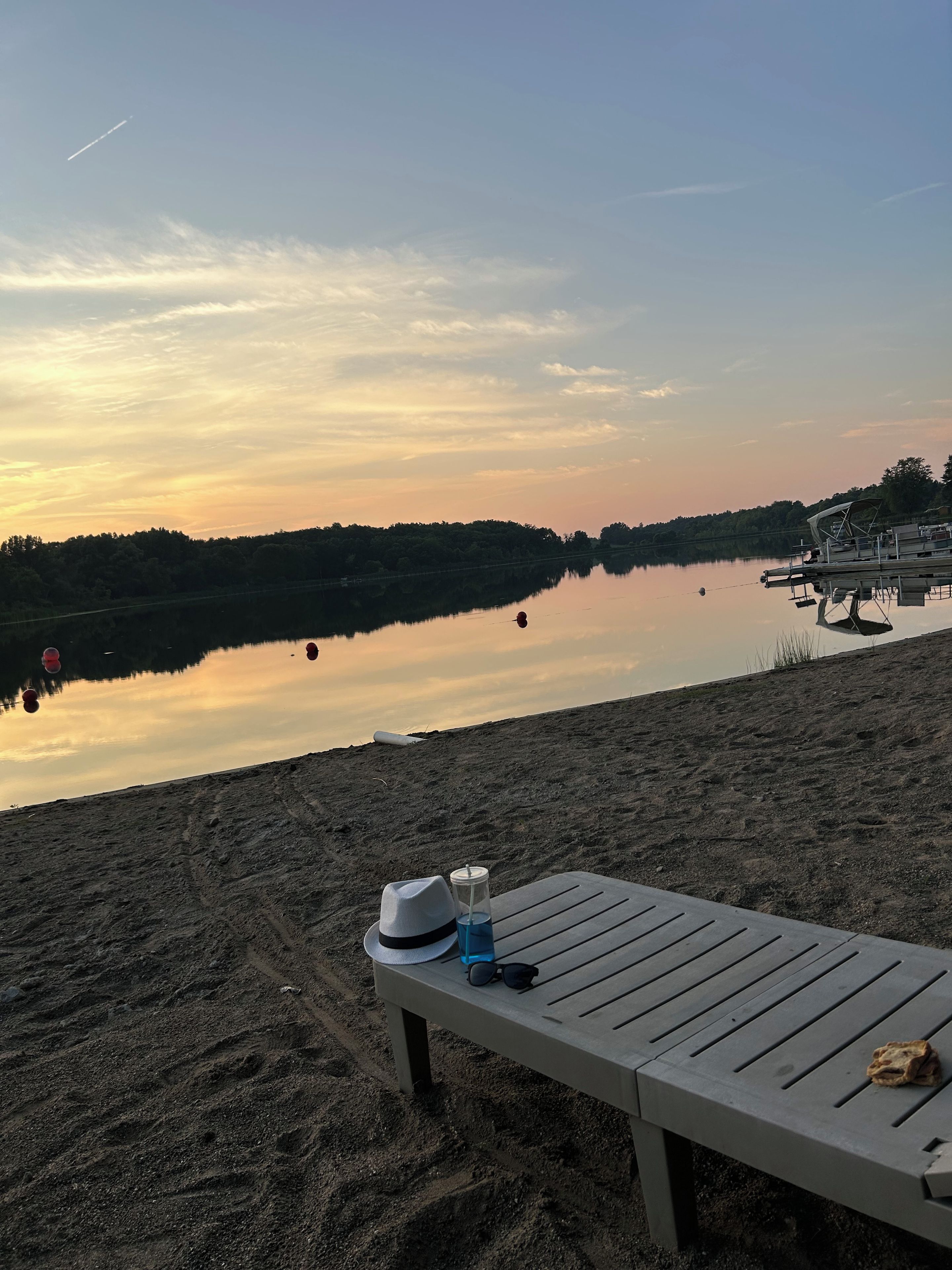Ranta, jossa on puinen aurinkotuoli, hattu, aurinkolasit ja juoma hiekalla.