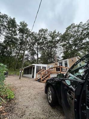 A modern house with a gravel driveway, a wooden staircase, and a black car parked in front.