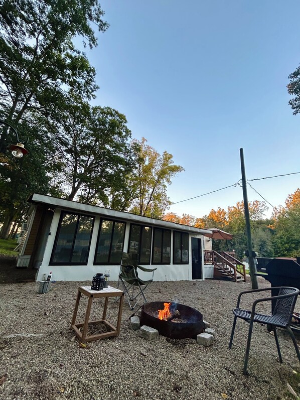 A modern building with large windows, a fire pit, outdoor seating, and a staircase leading to a deck.