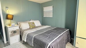 A bedroom with a bed, a nightstand, a lamp, a window with blinds, and a wardrobe. - Cozy cottage cabin with lake and beach access (Albion)
