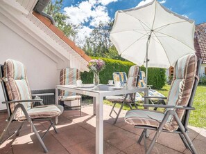 An outdoor patio with a table and chairs, a white umbrella, and a vase with flowers. - 5b/t5 Holiday Park "freesenbruch" (Zingst)