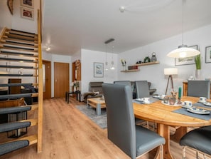 A modern living room with a wooden staircase, a dining area with a wooden table and chairs, and a sofa set. - 5b/t5 Holiday Park "freesenbruch" (Zingst)