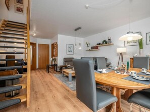 A modern living room with a wooden staircase, a dining area with a wooden table and chairs, and a sofa set. - 5b/t5 Holiday Park "freesenbruch" (Zingst)