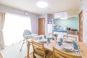 Een eethoek met een tafel voor vier personen, een kinderstoel en een keuken met een magnetron en fornuis.
