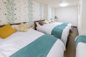 Een hotelkamer met twee bedden, elk met een blauwgroene spreidek, een geel kussen en een wit kussen. De kamer heeft behang met bloemenprint en een houten vloer.