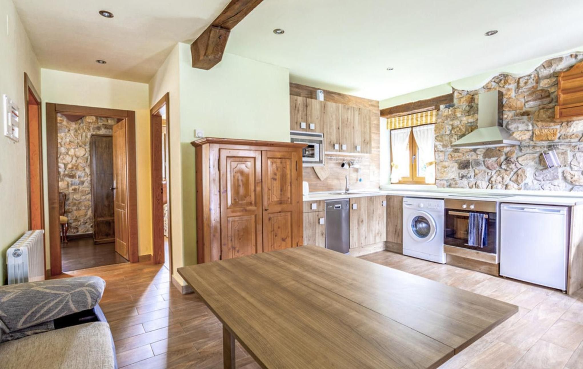 A kitchen with wooden cabinets, a dining table, and a stone wall.