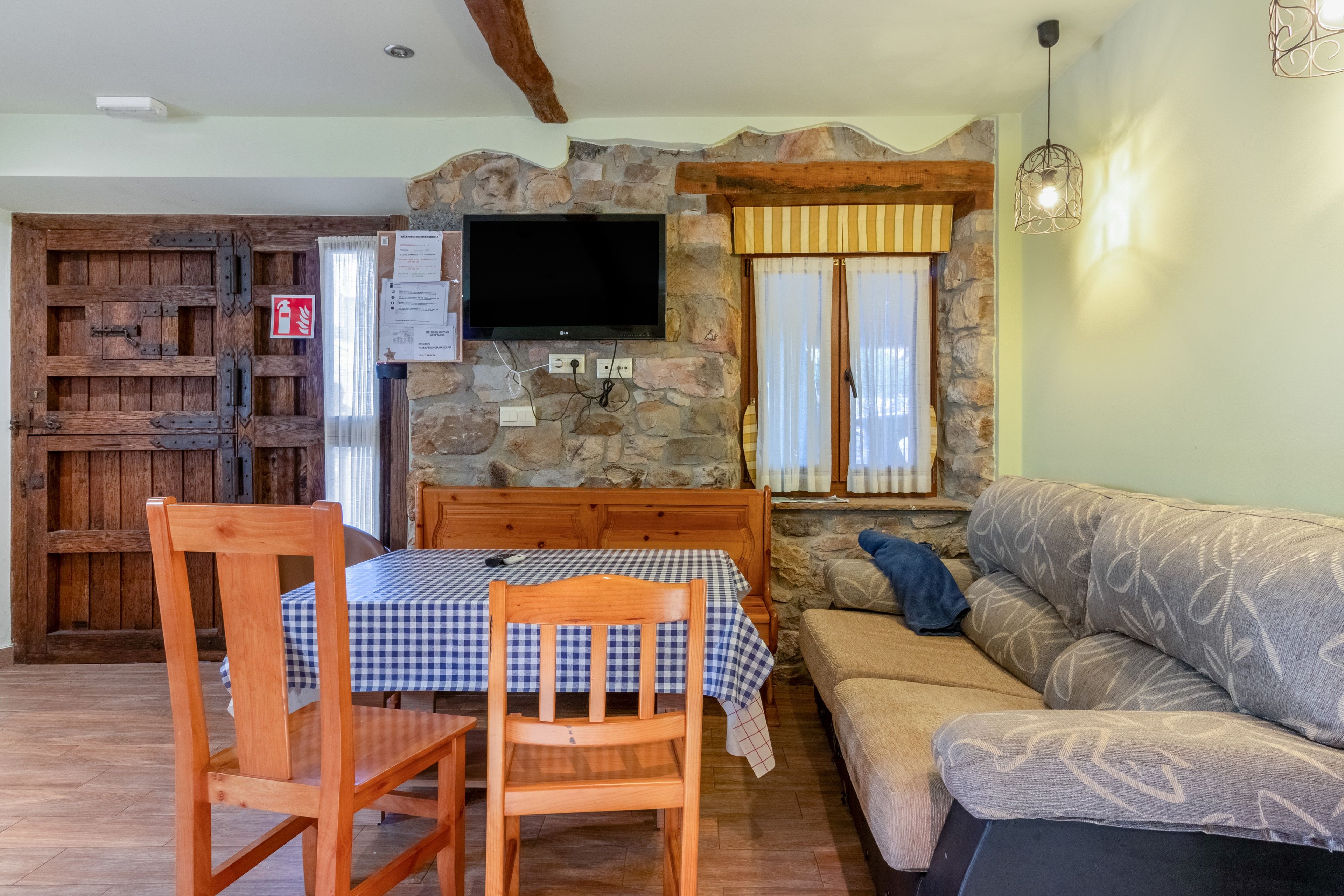 Una sala de estar acogedora con una pared de piedra, un televisor sobre la chimenea, una mesa de comedor de madera con sillas y un sofá.