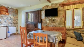 A cozy room with a stone wall, a flat-screen TV mounted on the wall, a wooden table with a checkered tablecloth, and a sofa with a cushion.