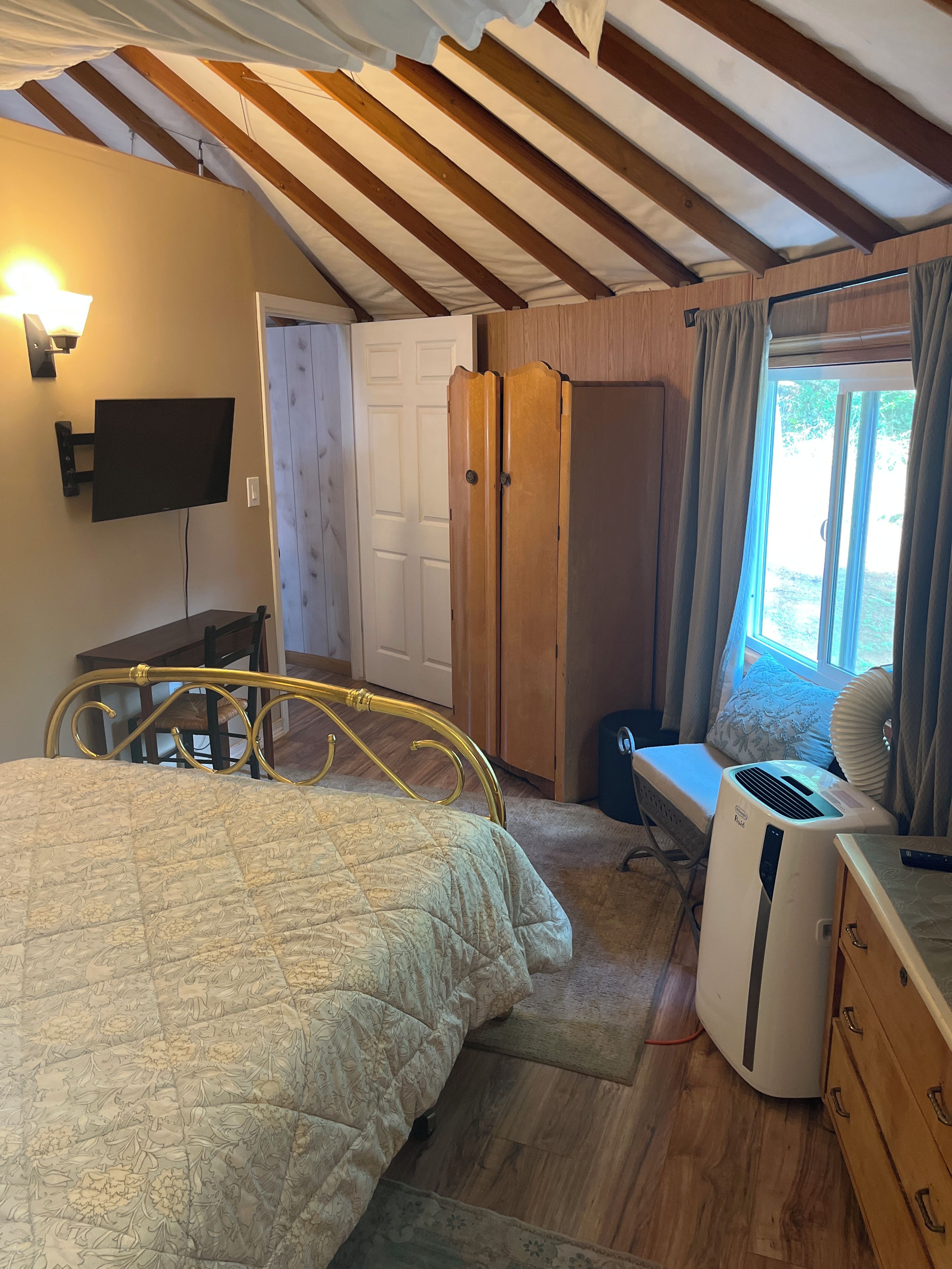 Une chambre à coucher avec un lit, un téléviseur fixé au mur, une armoire et une fenêtre avec des rideaux.