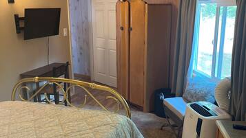 Une chambre à coucher avec un lit, un téléviseur fixé au mur, une armoire et une fenêtre avec des rideaux.