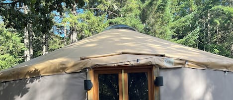 A wooden deck leading to a yurt with a door and windows, surrounded by trees.