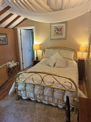 Un dormitorio con una cama con dosel, un aparador de madera, una mesita de noche con una lámpara y un cuadro enmarcado en la pared.