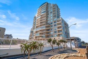 Um edifício residencial de vários andares com varandas, cerca branca e palmeiras.