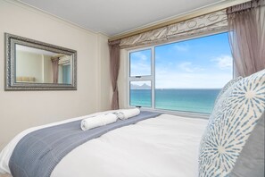 Quarto de hotel com uma cama grande, vista para o mar, um espelho e cortinas.