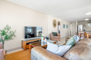 A living room with a television, sofa, coffee table, and a potted plant. - The Waves 704 - Two Bedroom Apartment, Sleeps 4 (Cape Town)